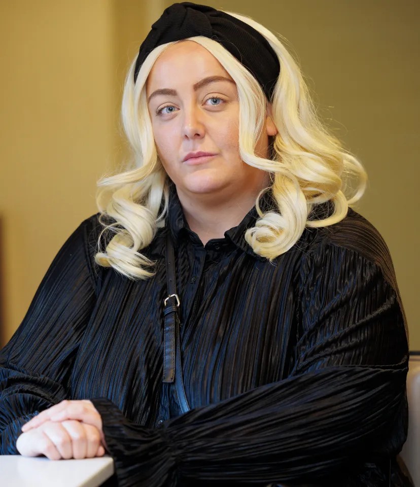 Woman with blonde hair and a black headband wearing a black pleated shirt.