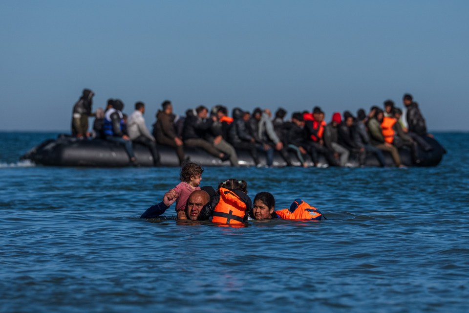 Migrant family in the water, approaching a boat full of other migrants.