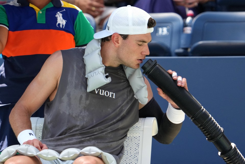 Sweaty tennis player Jack Draper drinks from a cooling device.
