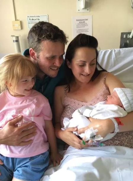 Family photo in hospital room with newborn baby.