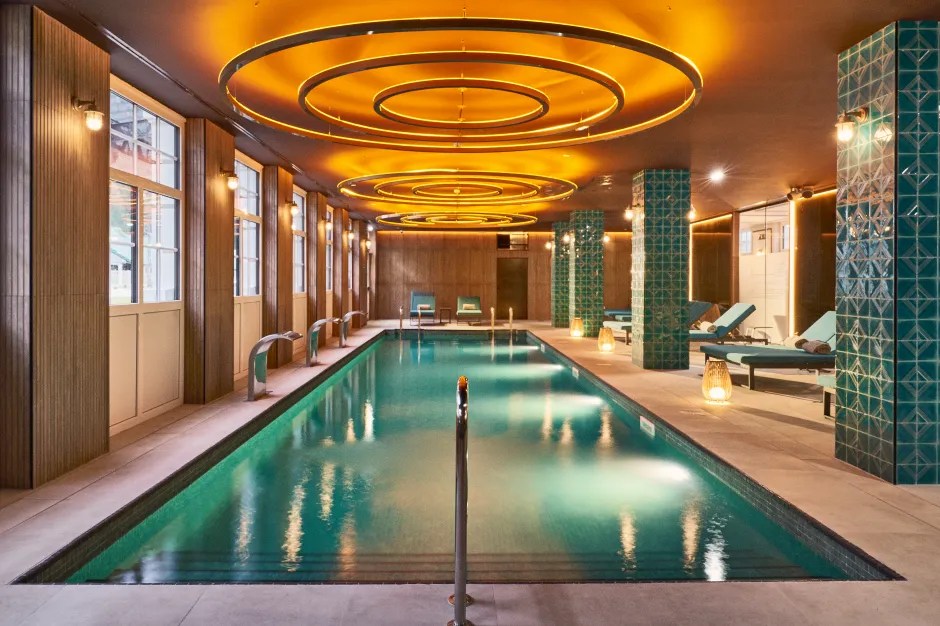 Indoor swimming pool with teal water and lounge chairs.