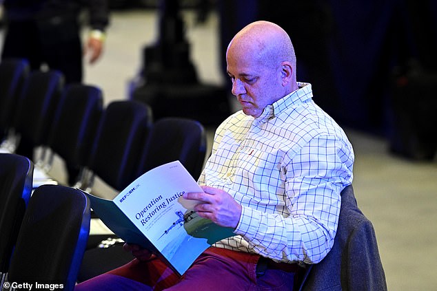 An audience member reads Reform's 'Operation Restoring Justice' plans while waiting for Mr Farage's speech to begin