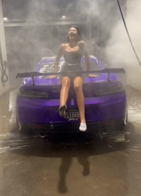 Woman sitting on the back of a purple car in a car wash.