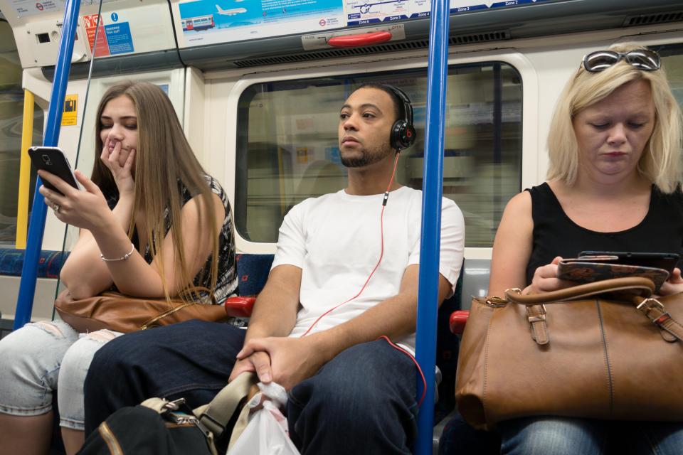 Passengers on a London Underground train using mobile phones and headphones.