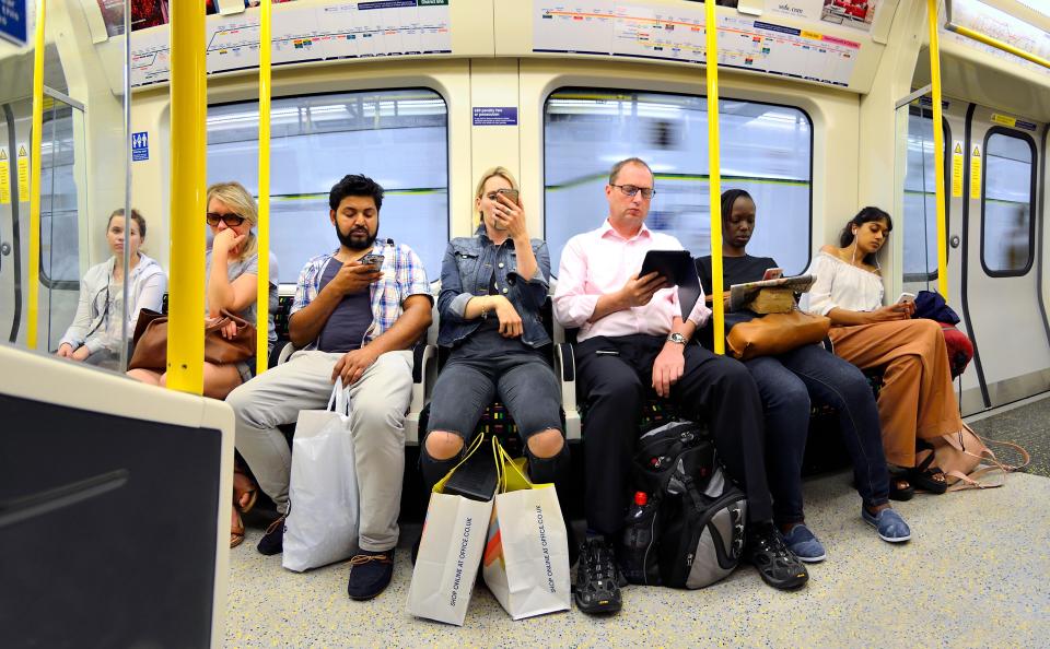 Passengers on a London Underground train using mobile phones and tablets.