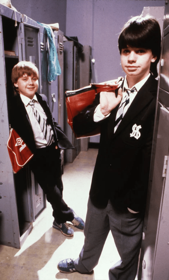 Two boys in school uniforms stand in a locker room.