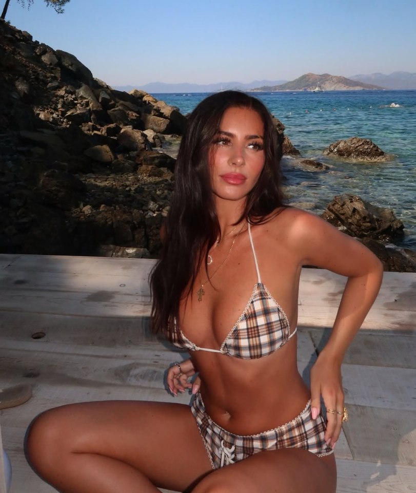 Woman in a plaid bikini sitting on a dock by the ocean.