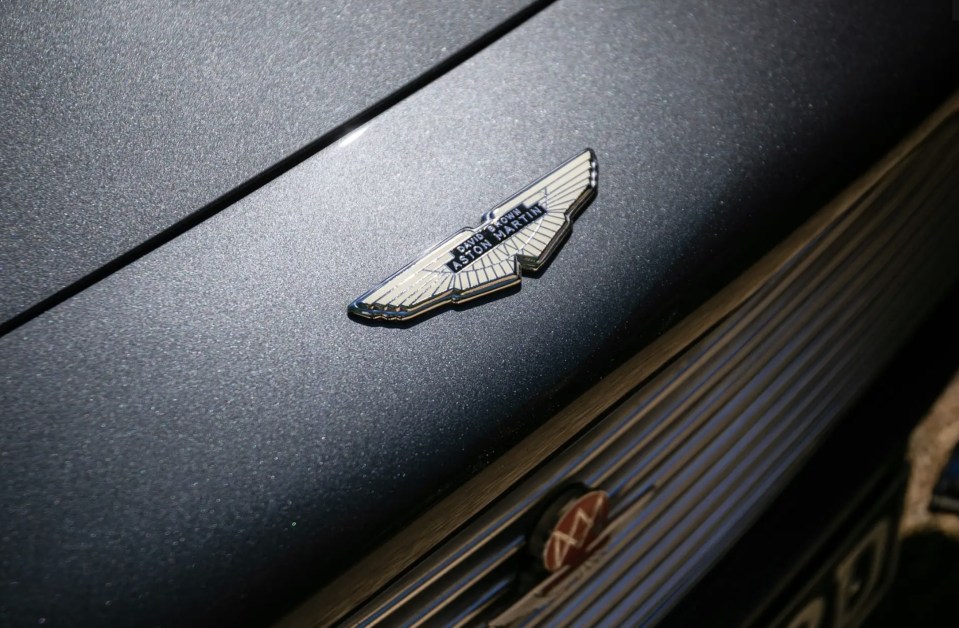 Close-up of an Aston Martin logo on a slate grey classic car.