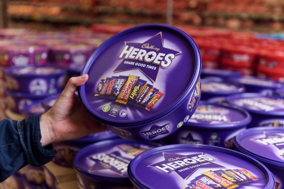 A hand holding a tub of Cadbury Heroes chocolates.