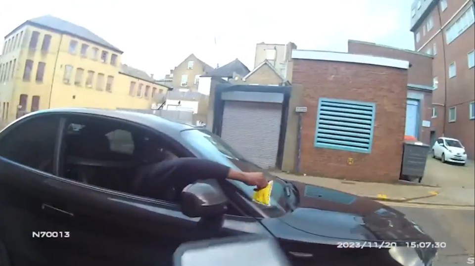 Person placing parking ticket on car windshield.