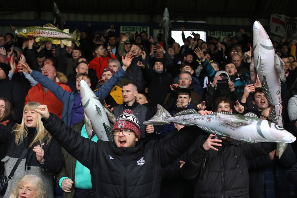 Grimsby Town fans holding inflatable haddock at a soccer match.