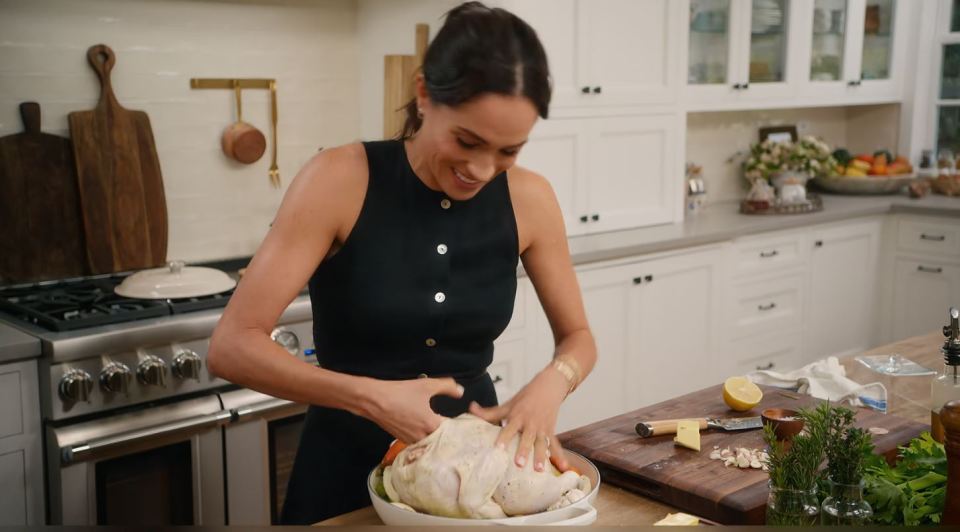 Meghan Markle preparing a roast chicken in a kitchen.