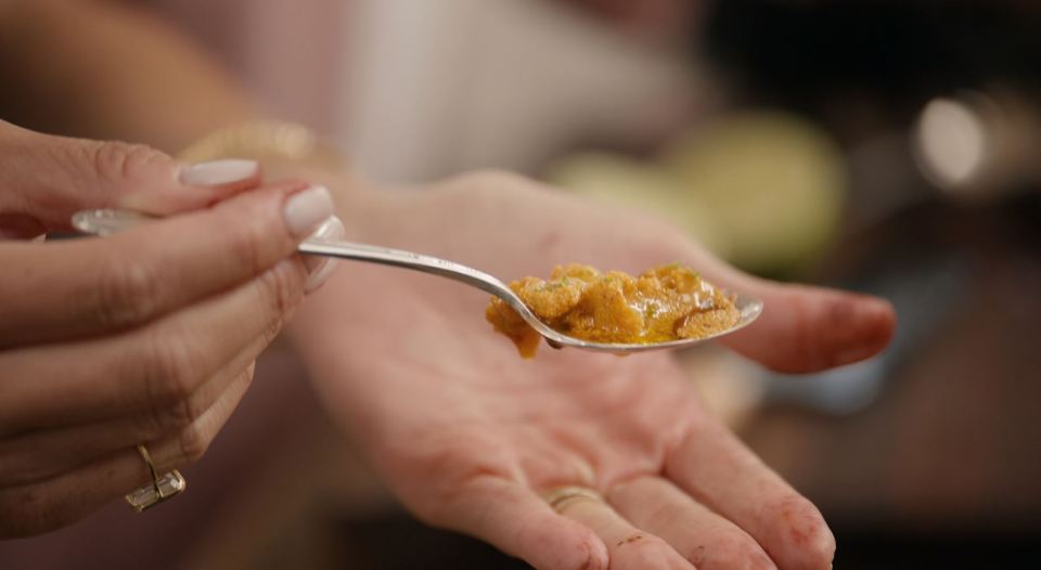 Spoon of orange food held over a hand.