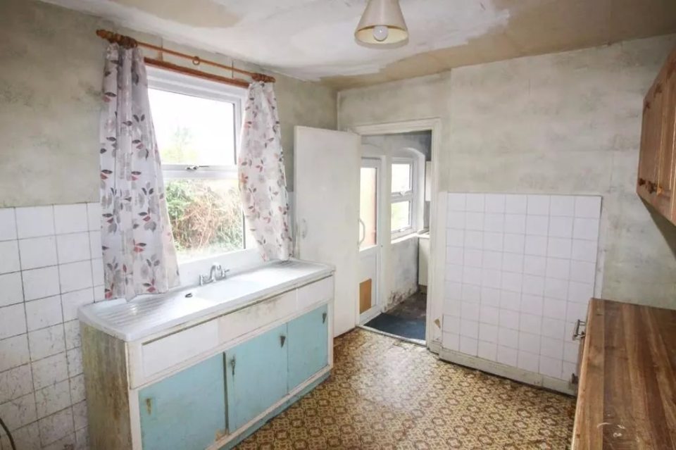 A dated kitchen with light blue cabinets and a floral curtain.