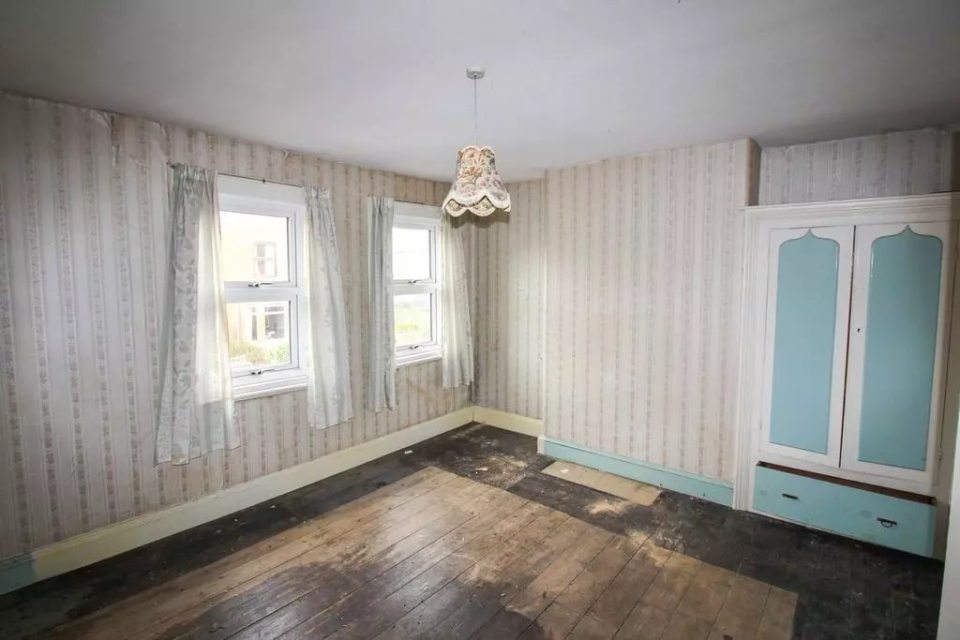 Empty room with damaged wooden floor, patterned wallpaper, and a light fixture.