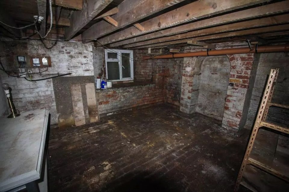 A dirty, unfinished basement with exposed brick walls and a low ceiling.