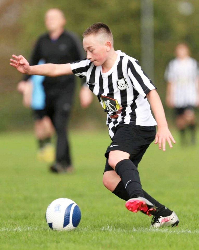 A boy in a soccer uniform kicking a soccer ball.