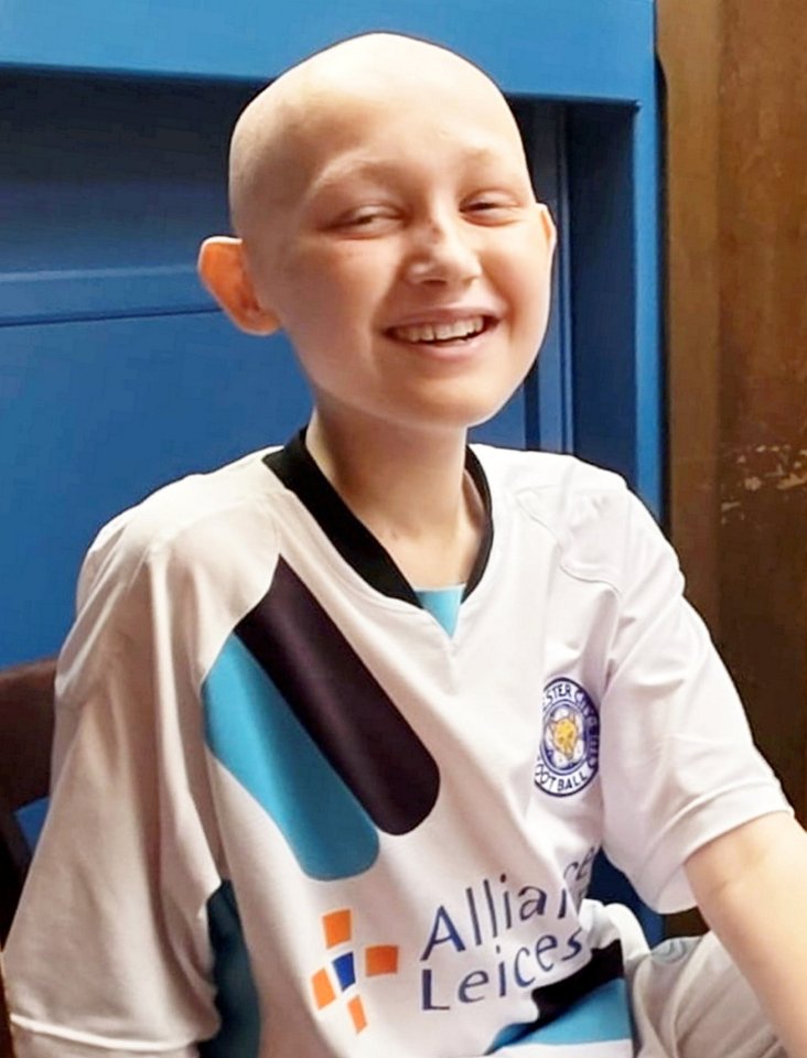 Smiling boy with shaved head wearing a Leicester City football shirt.