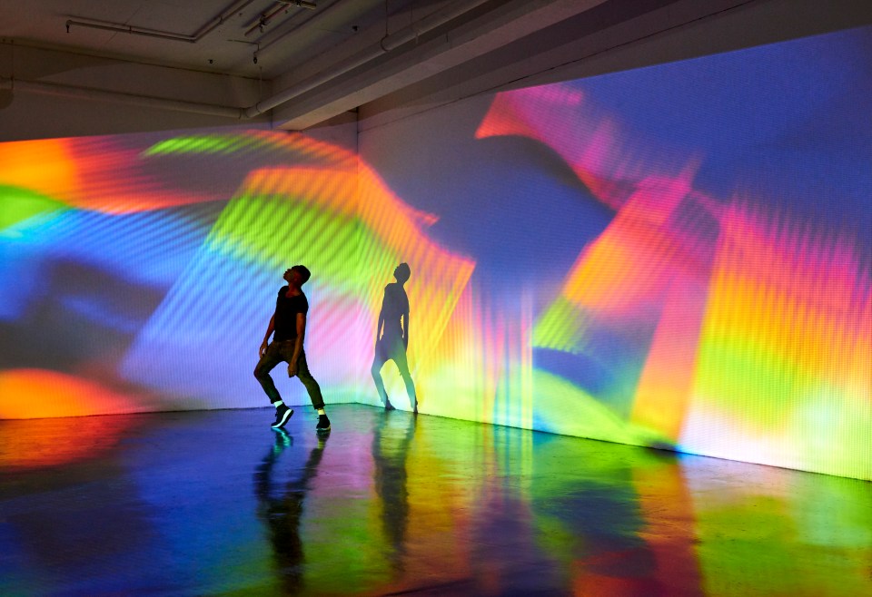 Man dancing against a wall with a colorful projection.