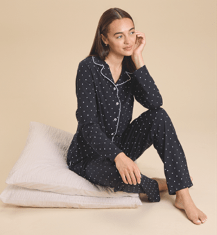Woman sitting on pillows wearing dark pajama set with white polka dots.