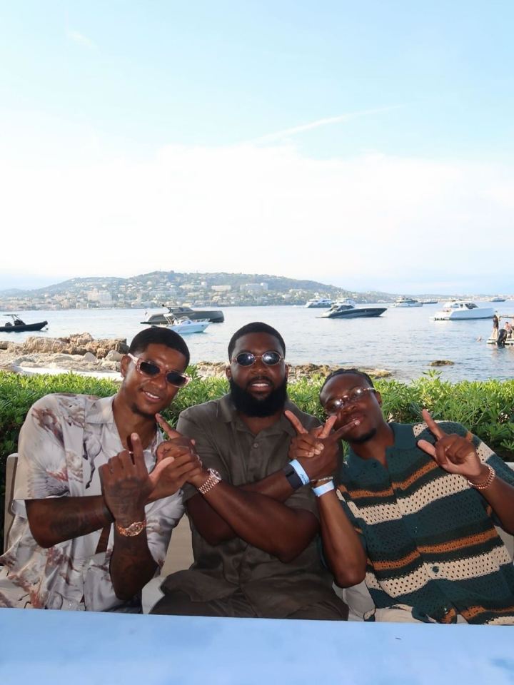 Three men posing outdoors with a waterfront in the background.