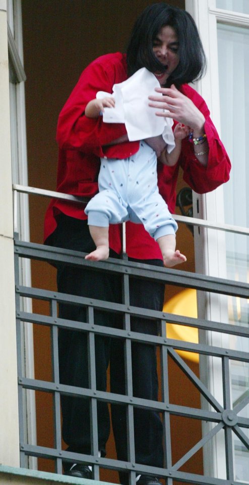 Michael Jackson holding a baby on a balcony.