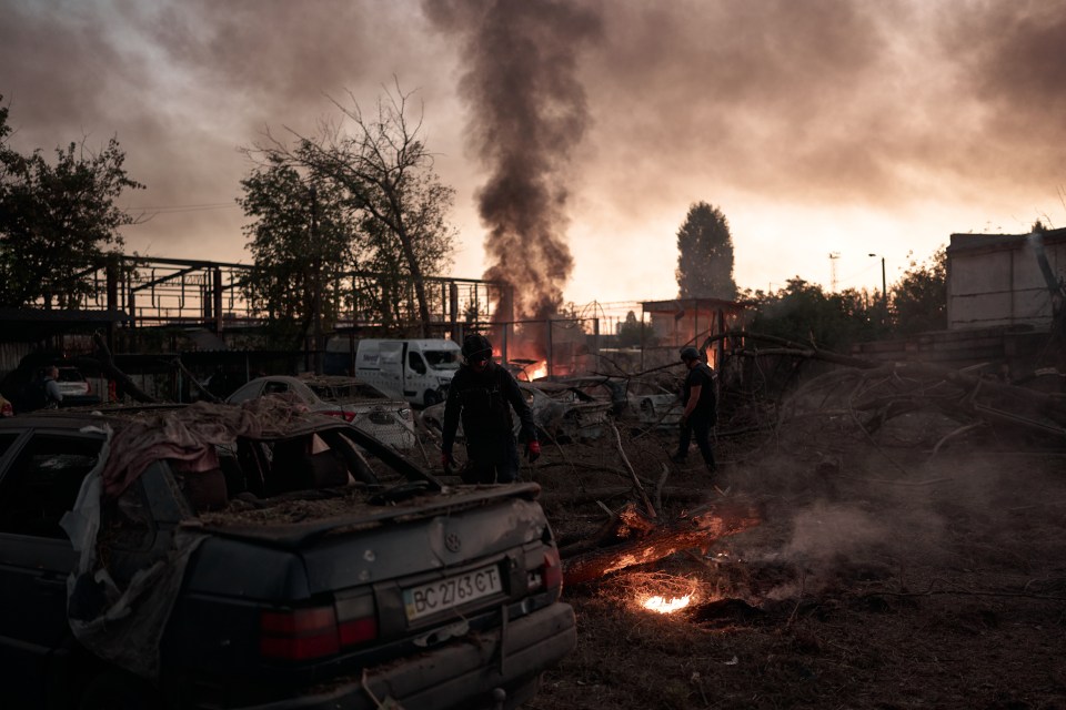 Aftermath of a missile strike in Kyiv, Ukraine, showing rescuers amidst damaged cars and burning debris.