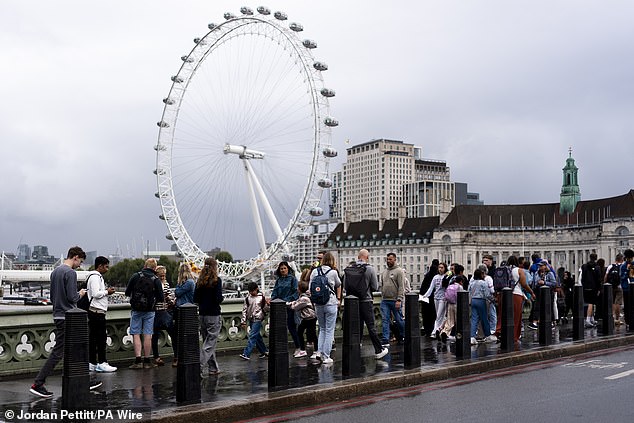 Pedestrians walk in front of the London Eye in Westminster on a wet day yesterday