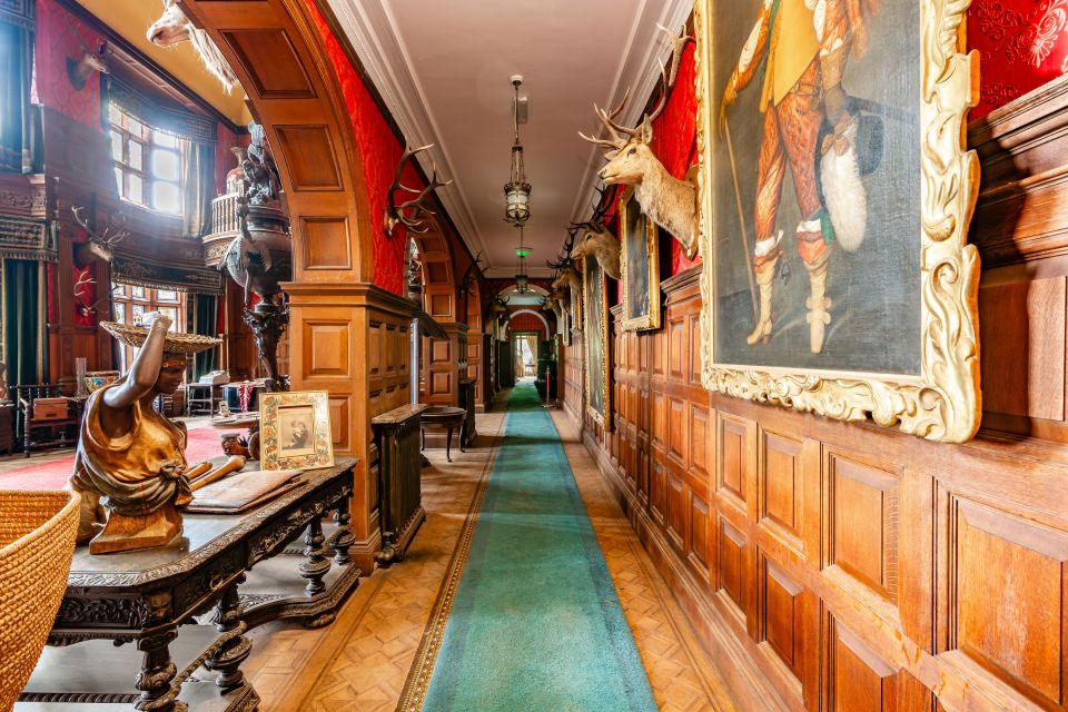 Interior of Kinloch Castle hallway with wooden paneling, taxidermied deer heads, and paintings.