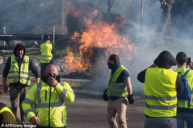 Protestors wearing a yellow vest (gilet jaune) stand next to a burning barricade as they demonstrate against rising costs of living they blame on high taxes at the A9 highway toll of Le Boulou, southern France on December 22, 2018