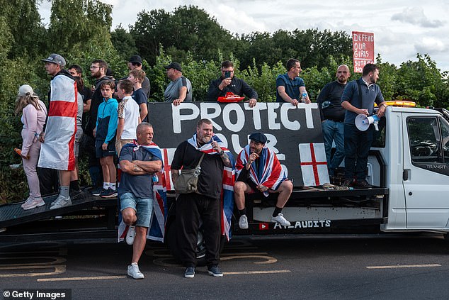 Demonstrators gathering outside the Bell Hotel on July 20, 2025, in Epping, England perched against a sign that says 'Protect Our Kids'