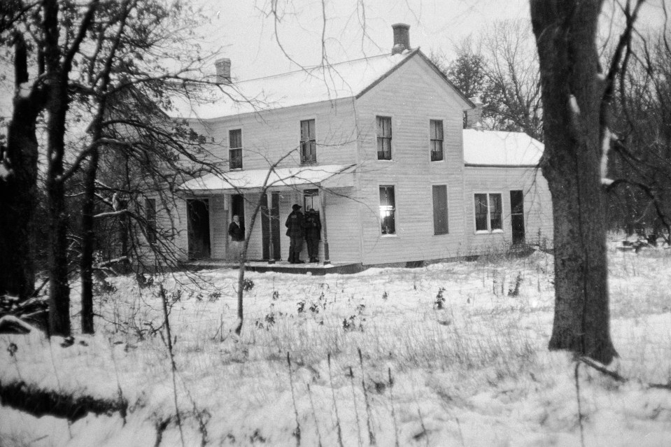Black and white photo of onlookers outside Ed Gein's house in winter.