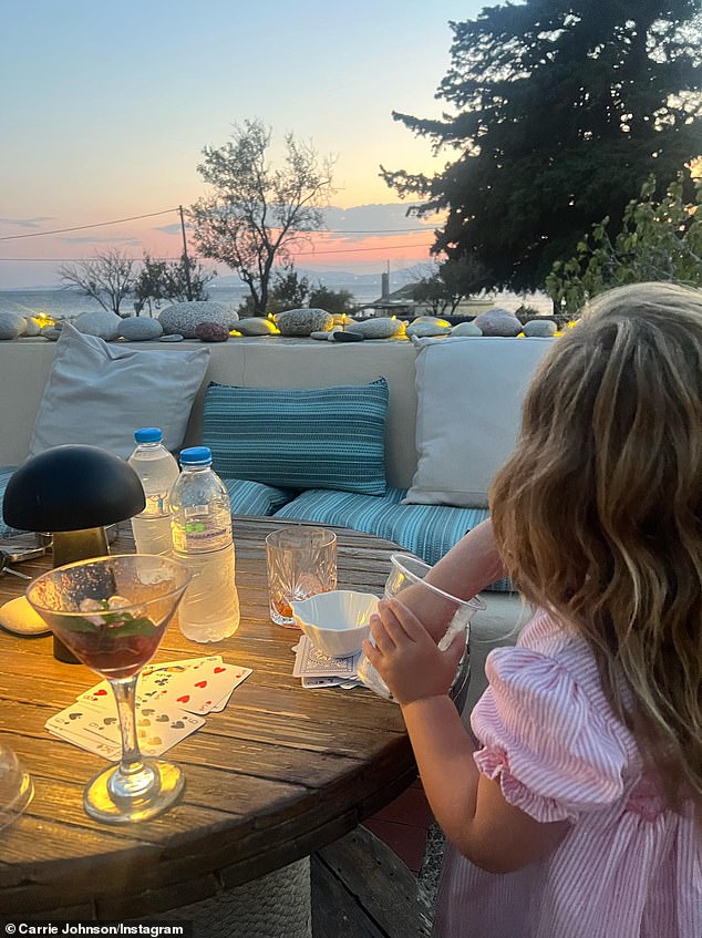 Romy puts her hand into a cup while sitting at a table during the family's summer holiday