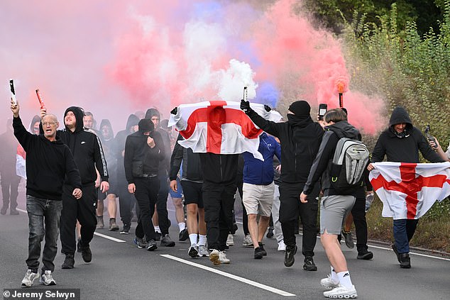 Demonstrators - some hooded and masked - let off flares into the sky, while carrying England flags