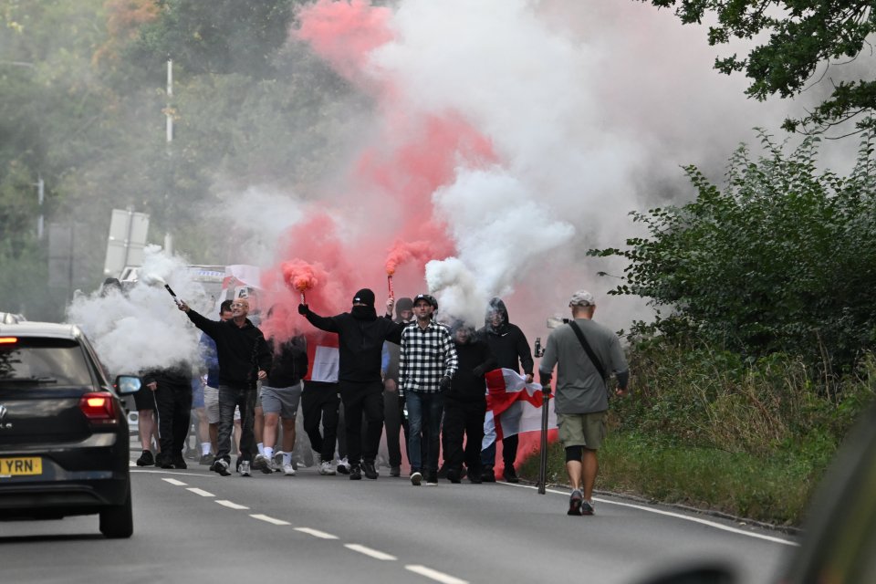 Demonstrators with red and white smoke flares march down a road.