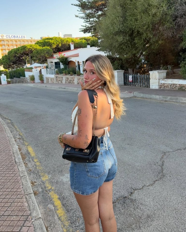 Woman in denim shorts and white halter top, looking over her shoulder.