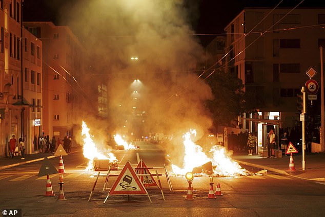Burning containers block the street during the third night of riots in Lausanne, Switzerland, Tuesday August 26, 2025