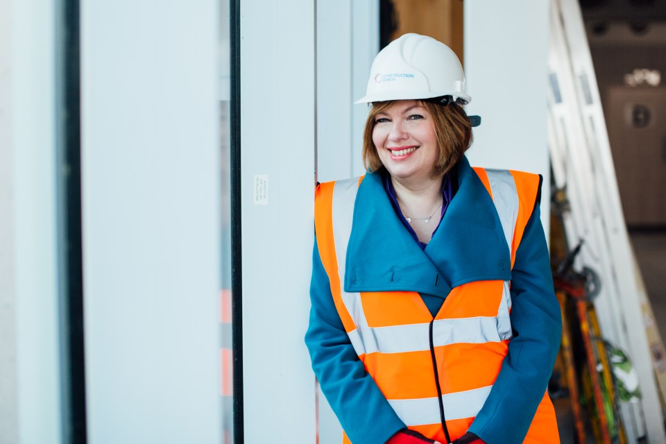 Woman in hard hat and safety vest smiling.