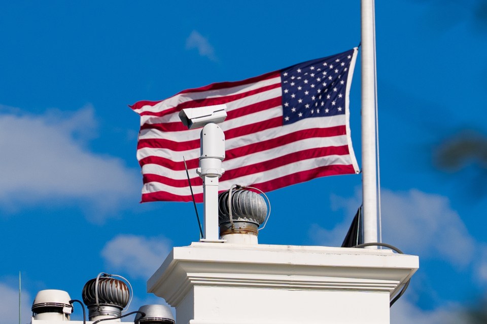 US flag at half-staff over a security camera.