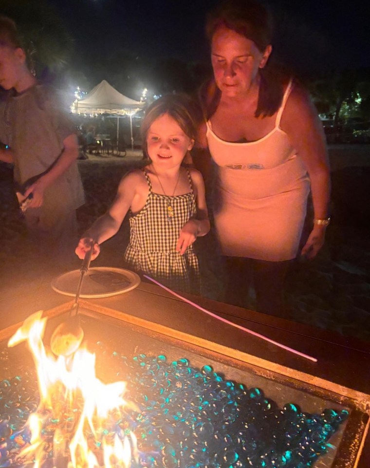 A young girl and woman roasting marshmallows over a fire pit.