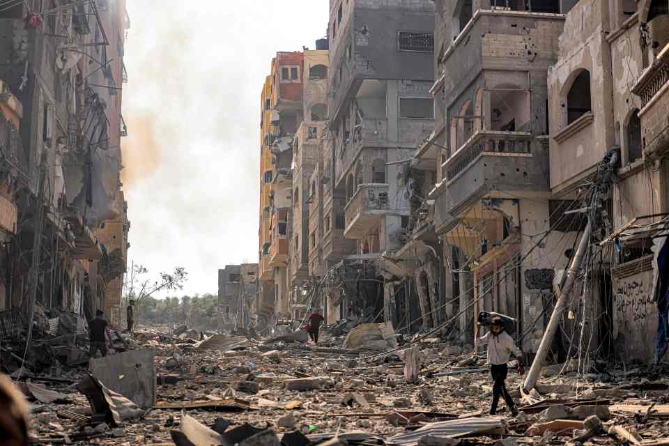 A man carrying a gas cylinder walks through rubble in a war-torn street in Gaza.