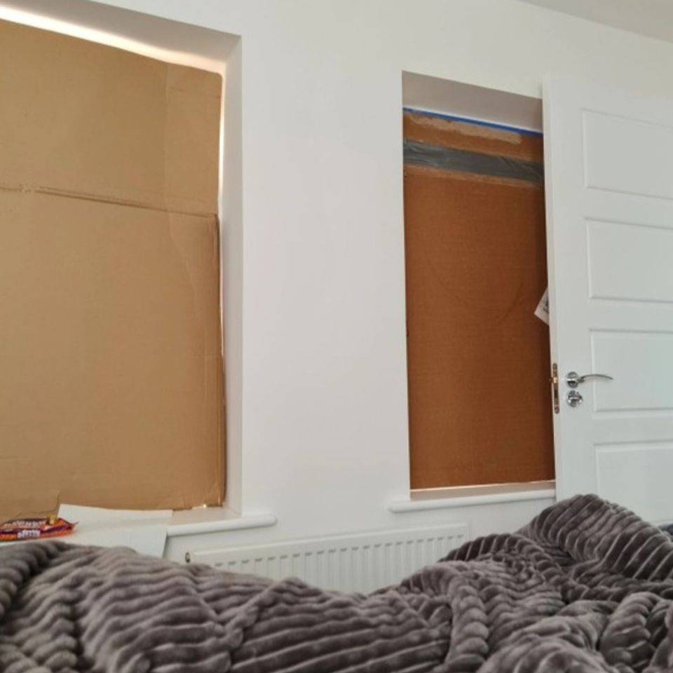 Windows covered with cardboard in a bedroom.