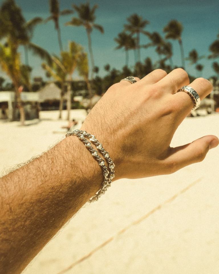 Hand wearing bracelets and rings on a beach.