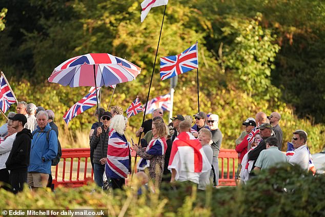 They also stand with British flags on their umbrellas amid fury after a judge ruled asylum seekers can stay in The Bell Hotel in Epping