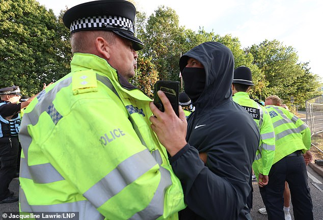 A masked man faces off with a police officer in Cheshunt outside the hotel believed to house migrants