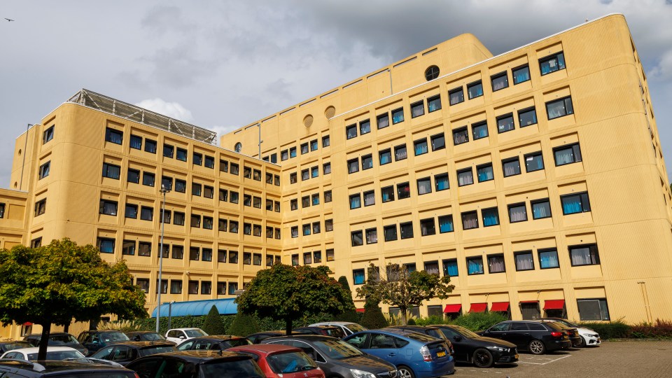 Large yellow hostel building with cars parked in front.