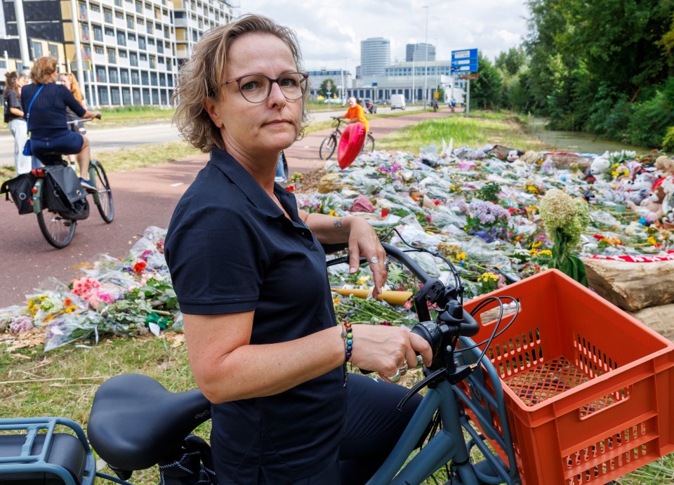 Woman on bicycle at a memorial with flowers and stuffed animals.