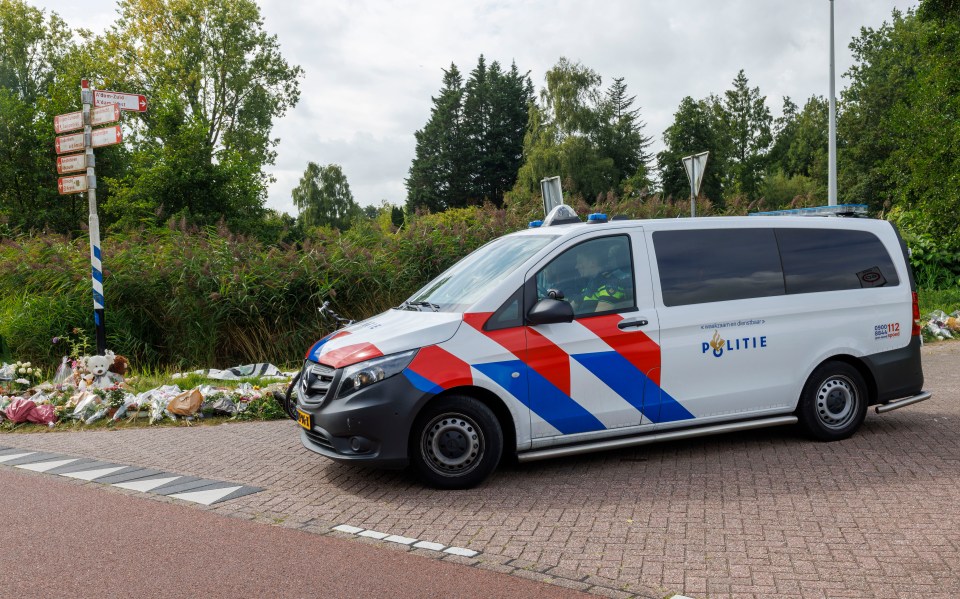 Tributes and a police van at a crime scene.