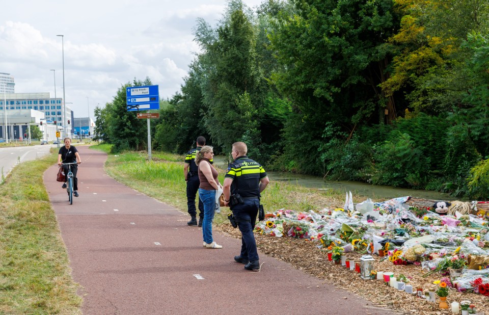 Police officers stand near a memorial of flowers and other tributes left at a bicycle path.