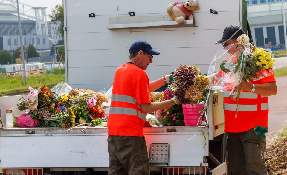 Two workers placing floral tributes into the back of a truck.